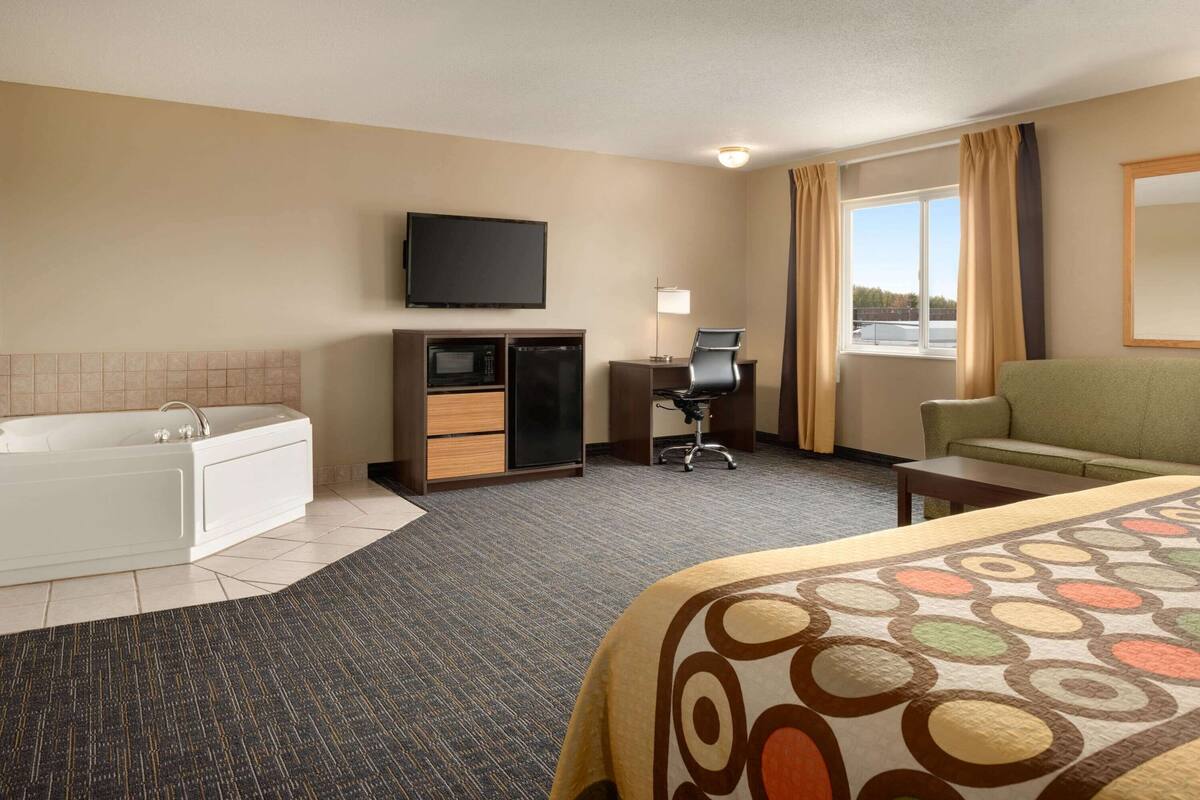 Une chambre d’hôtel équipée d’un lit, d’un bureau, d’une chaise, d’une télévision, d’un four à micro-ondes, d’un mini-réfrigérateur, d’une baignoire et d’une fenêtre avec des rideaux.