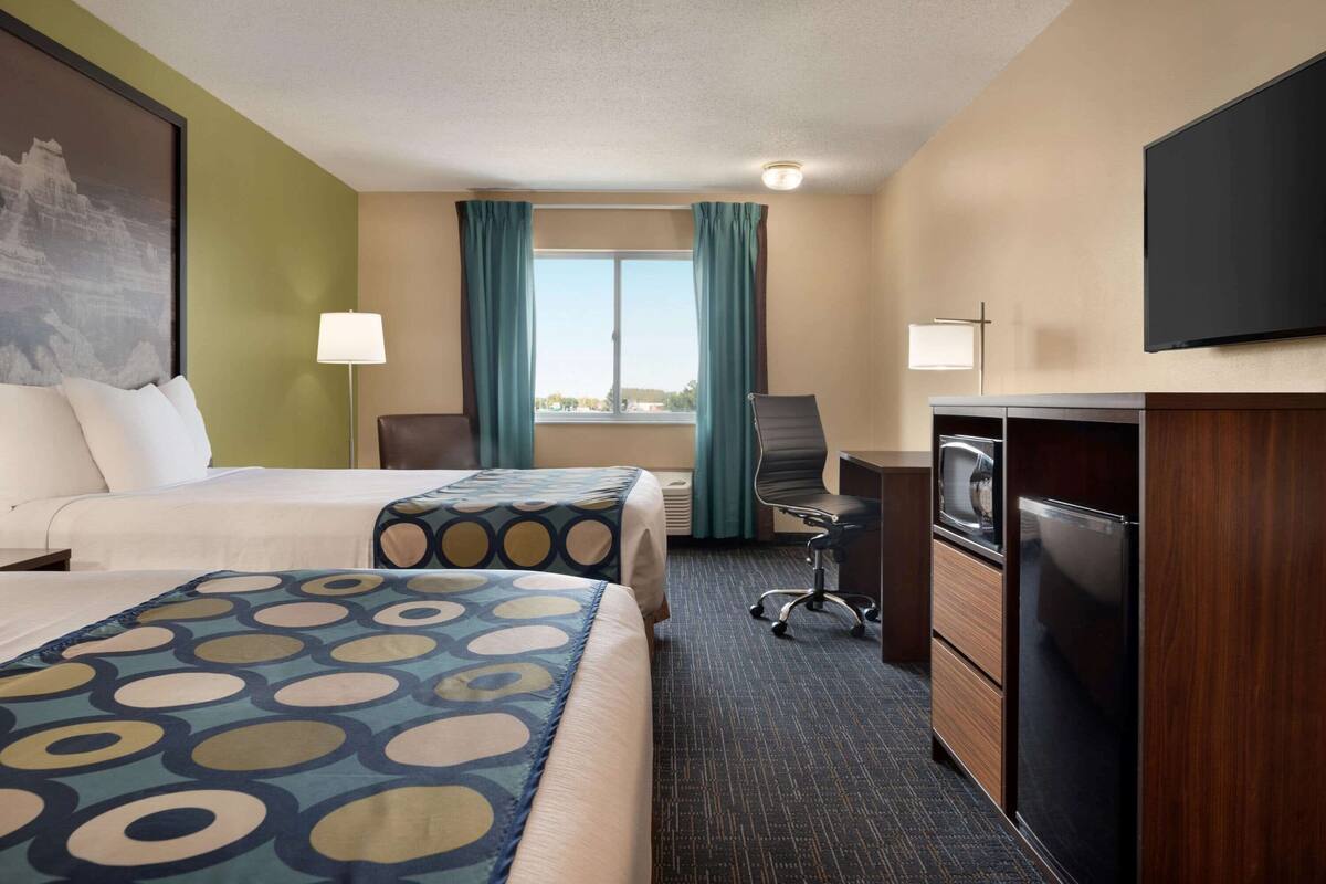 Une chambre d’hôtel avec deux lits, un bureau avec une chaise, un téléviseur à écran plat et un réfrigérateur.