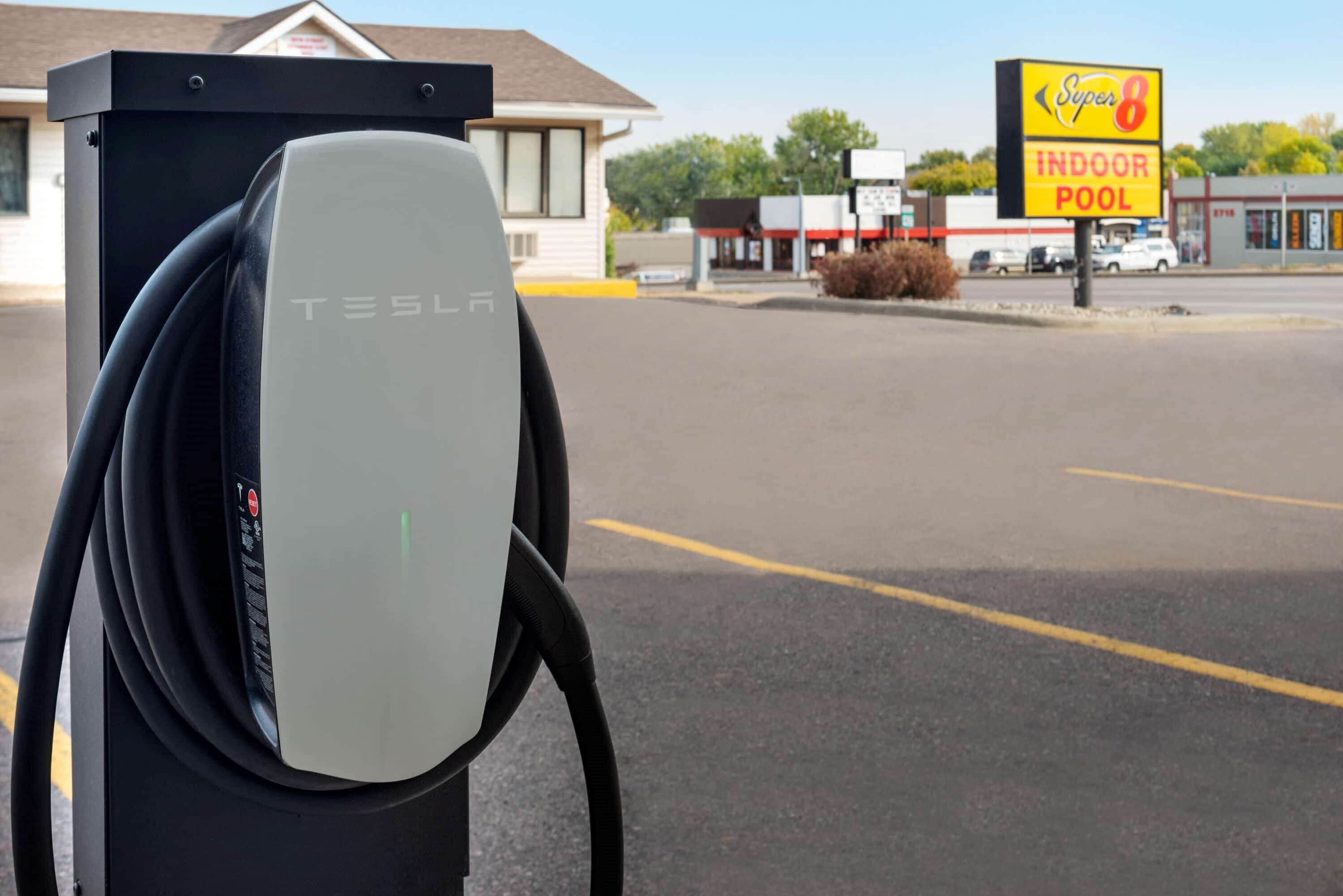 Una estación de carga de Tesla con un letrero de alberca techada Super 8 al fondo.