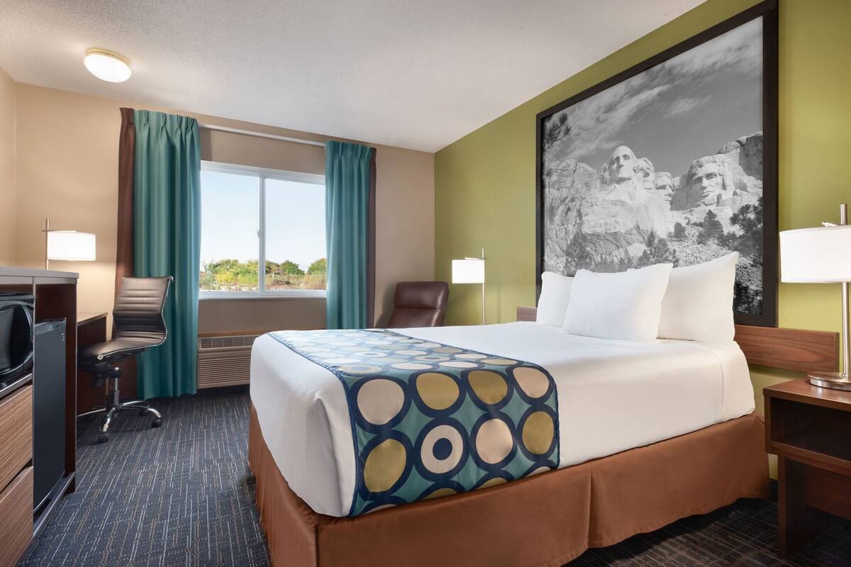 Une chambre d’hôtel avec un lit, un bureau, une chaise et une grande fenêtre.