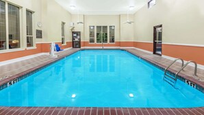 Una piscina con agua azul cristalina, rodeada por una terraza con baldosas y paredes pintadas en tonos beige y naranja.