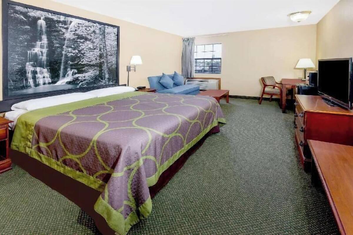 Quarto de hotel com uma cama grande, uma escrivaninha, uma cadeira, uma televisão e um quadro grande na parede.