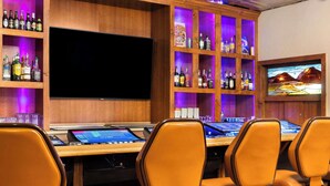 A bar area with a large flat-screen TV, wooden shelves with liquor bottles, and orange chairs. - Super 8 by Wyndham Fallon (Fallon)