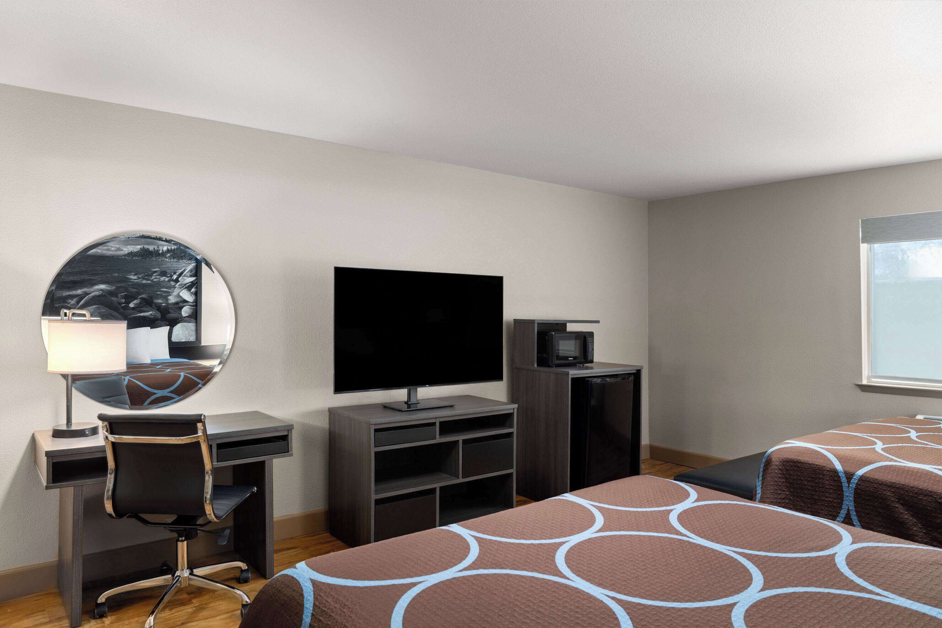 Habitación de hotel con escritorio, silla, televisor y dos camas con ropa de cama estampada.