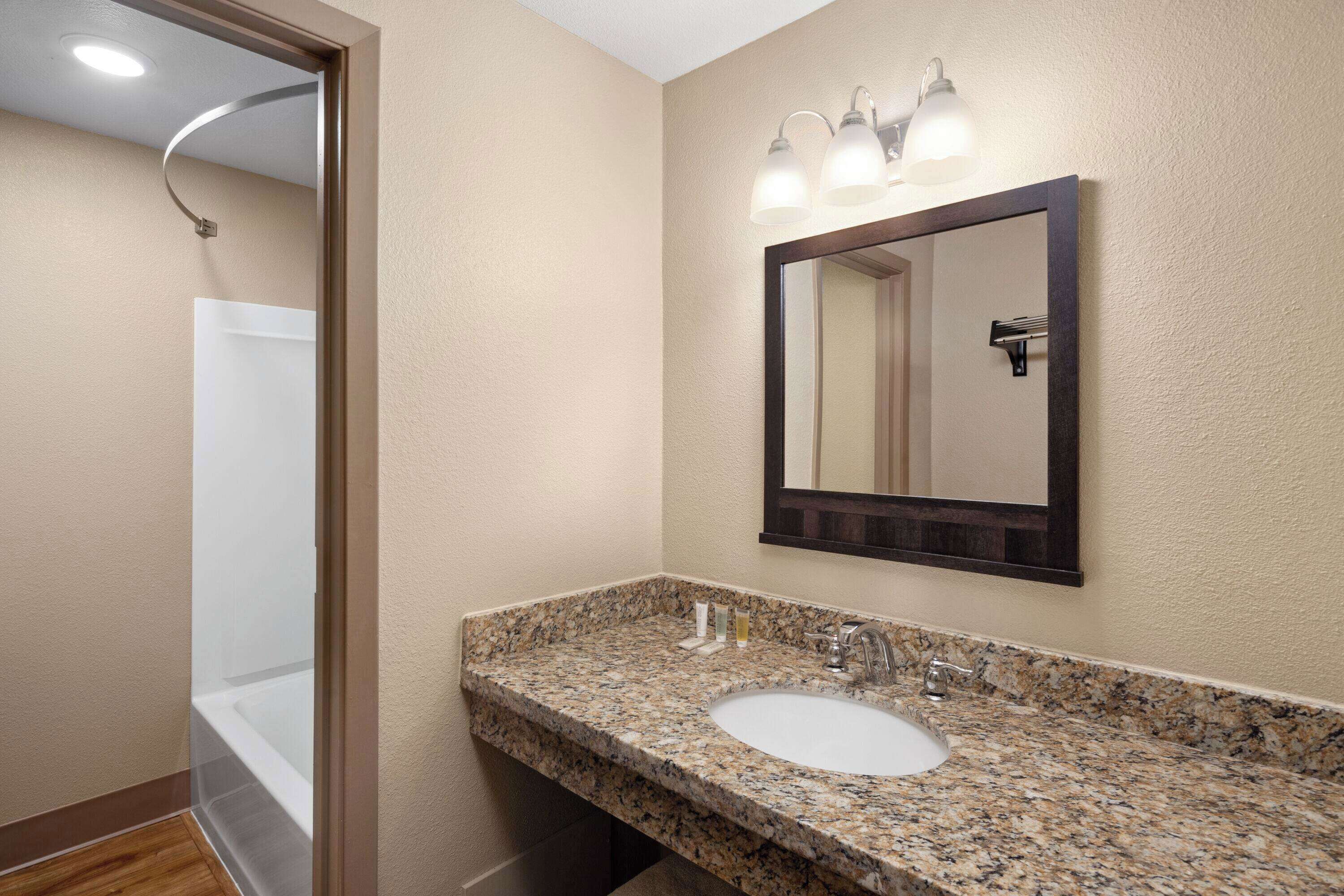 A bathroom with a granite countertop sink, a mirror, and a shower visible through an open door.