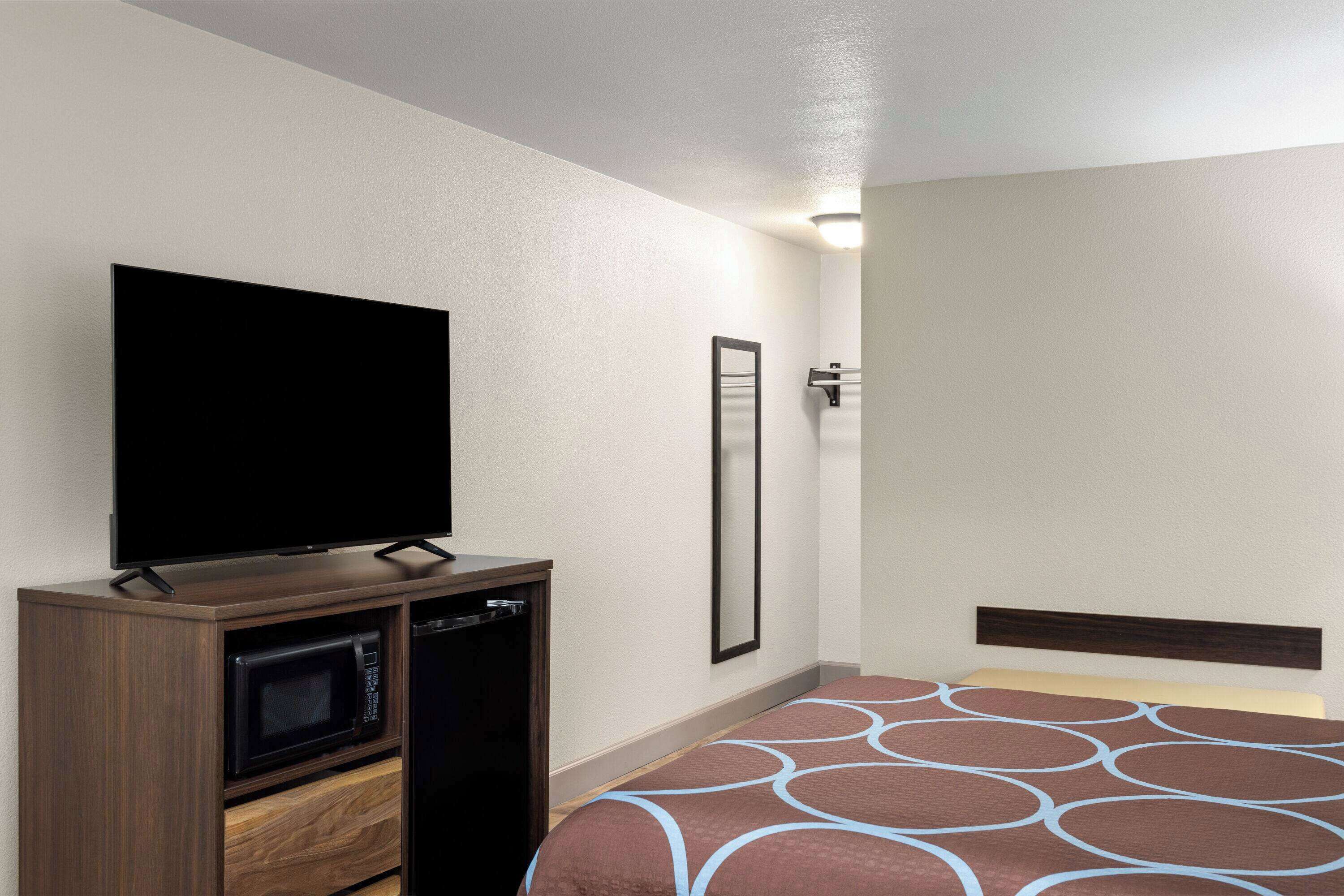 A hotel room with a bed, a television, a microwave, and a mirror.
