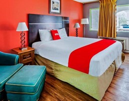 Habitación de hotel con cama, dos mesitas de noche con lámparas, ventana con cortinas y vista a un edificio.