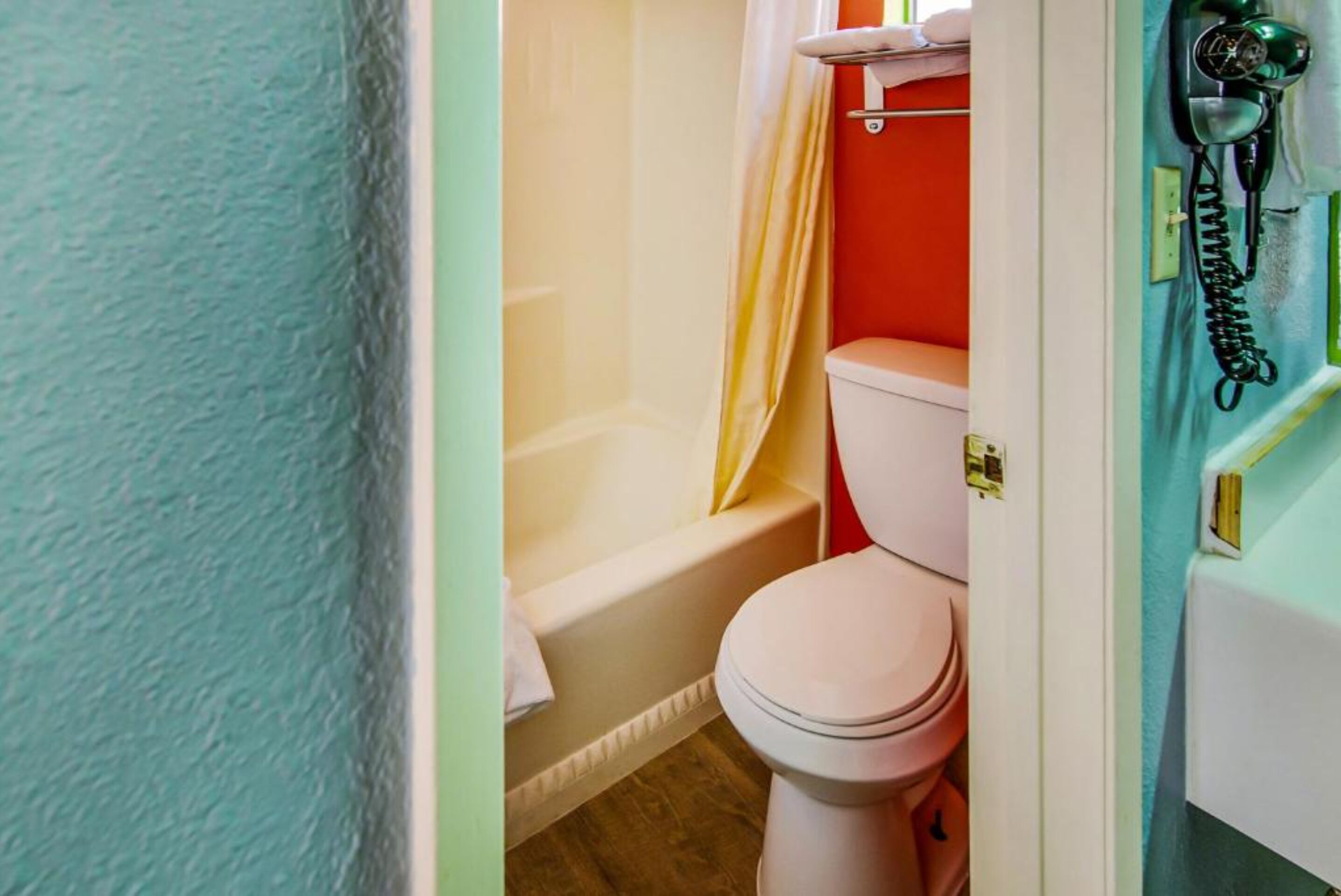 A bathroom with a white toilet, a bathtub, and a green telephone.
