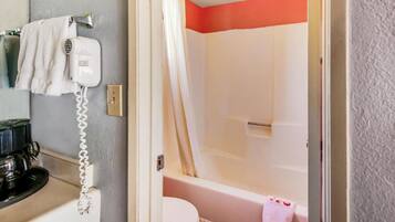 Un baño con inodoro blanco, ducha con cortina color beige y secador de pelo en la pared.