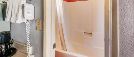 A bathroom with a white toilet, a shower with a beige curtain, and a hairdryer on the wall.