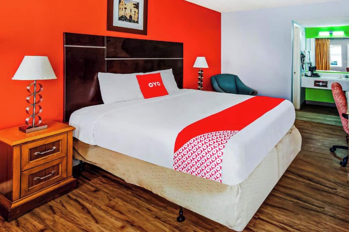 A hotel room with a large bed, two bedside tables with lamps, a wooden nightstand, a chair, and a desk with a chair.