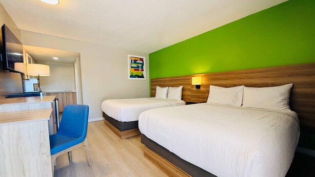 A hotel room with two beds, a desk with a chair, a green accent wall, and a small artwork. - Park Inn by Radisson, Quesnel (Quesnel)