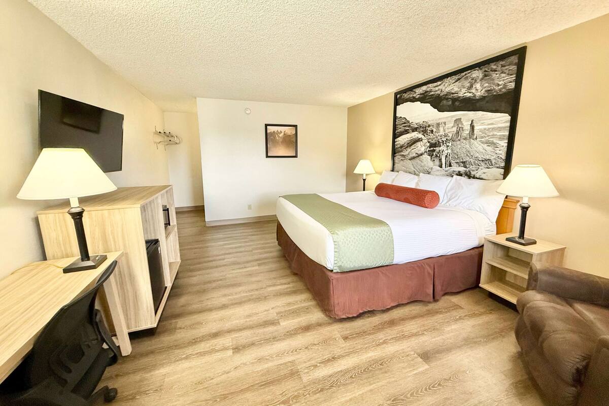 A hotel room with a bed, bedside tables, a desk, and a TV mounted on the wall.