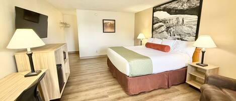 Una habitación de hotel con cama, mesitas de noche, escritorio y televisor montado en la pared.