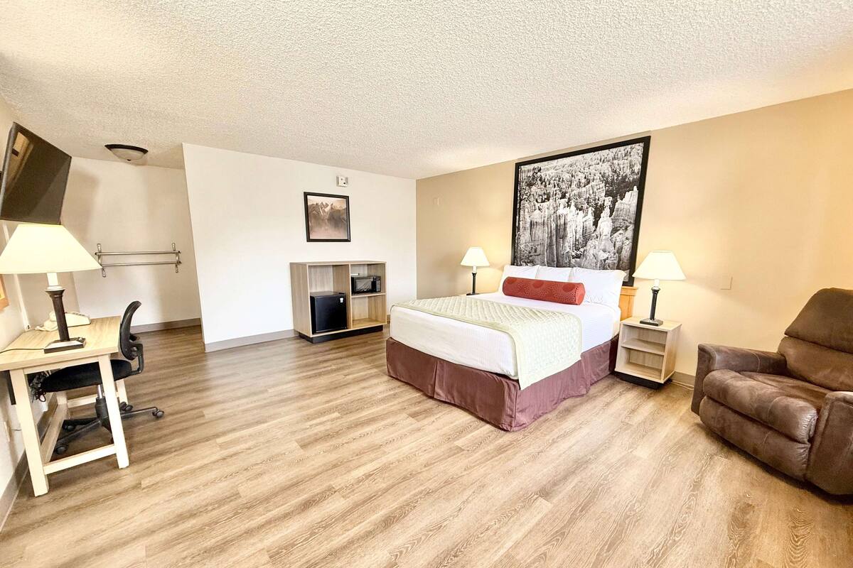 A hotel room with a bed, desk, chair, and a television.