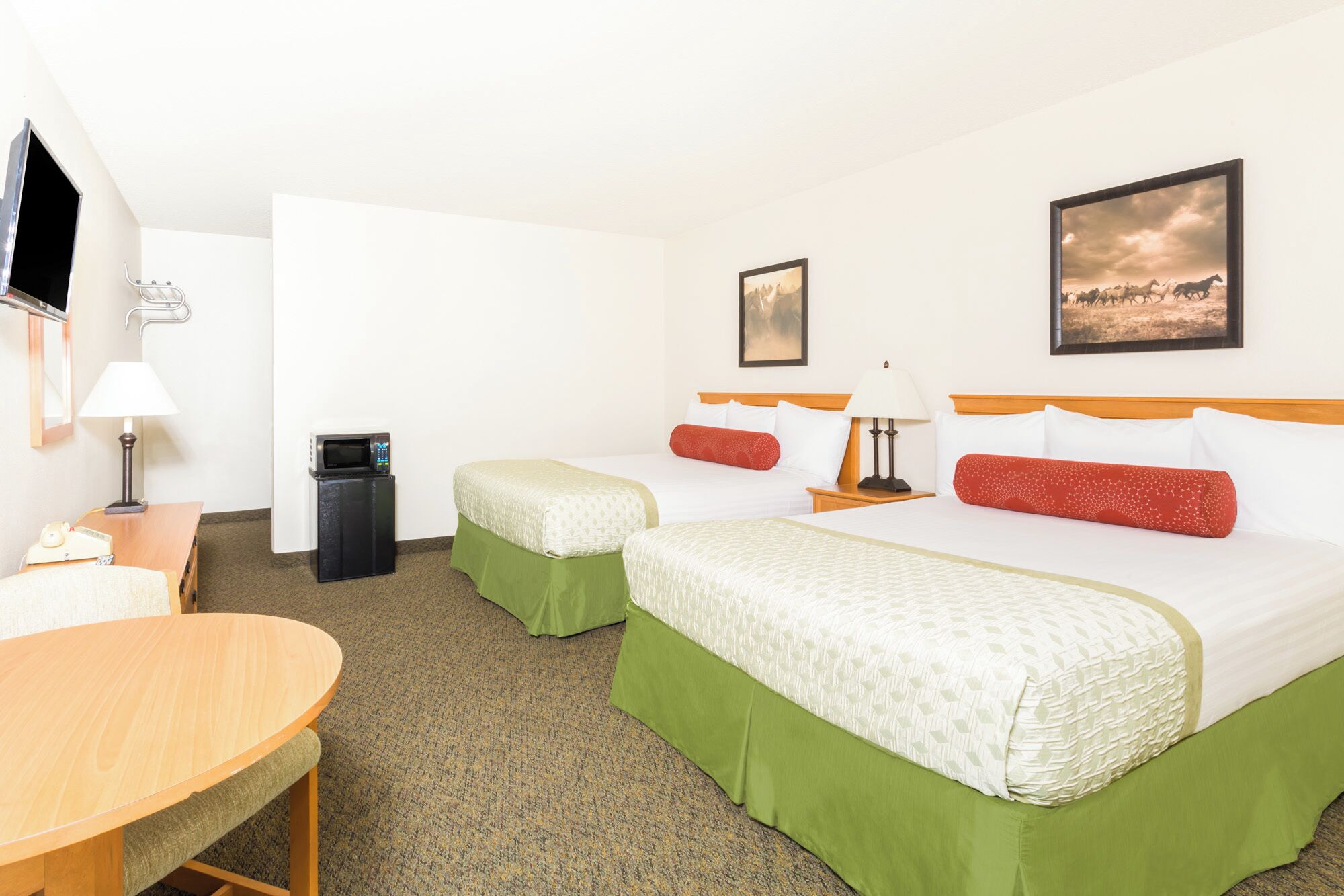 A hotel room with two beds, a desk, a chair, a TV, a microwave, and a trash bin.