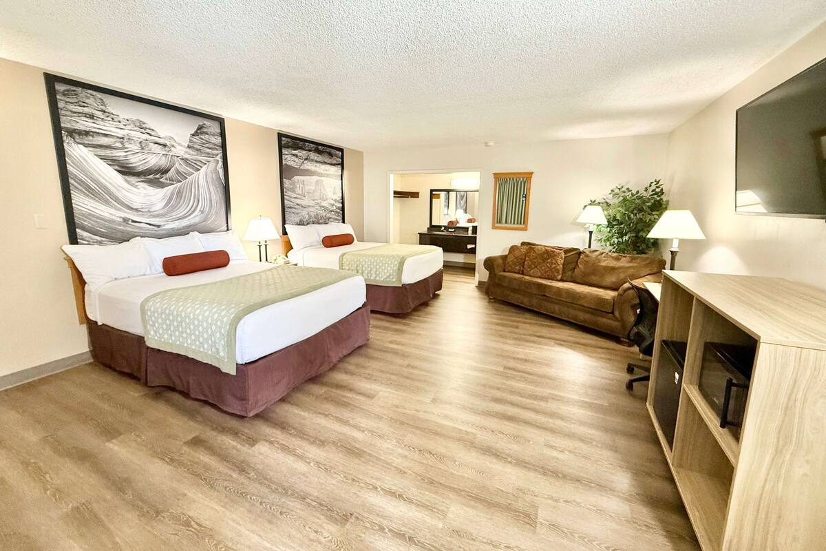 A hotel room with two beds, a sofa, a TV, and artwork on the walls.