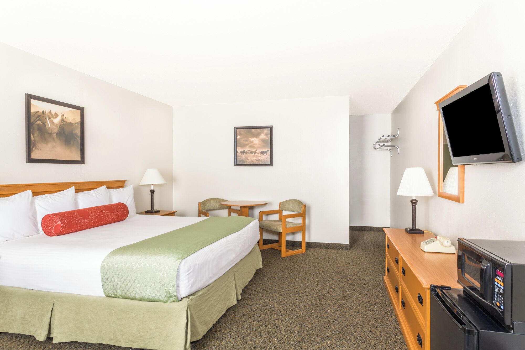A hotel room with a bed, two chairs, a desk, a television, and two wall-mounted lamps.