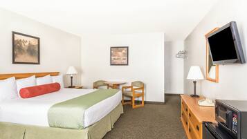 A hotel room with a bed, two chairs, a desk, a television, and two wall-mounted lamps.