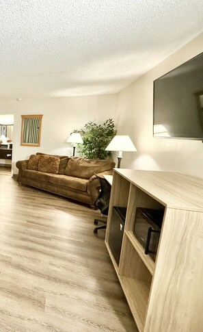 A living room with a sofa, a TV mounted on the wall, a lamp, and a plant.