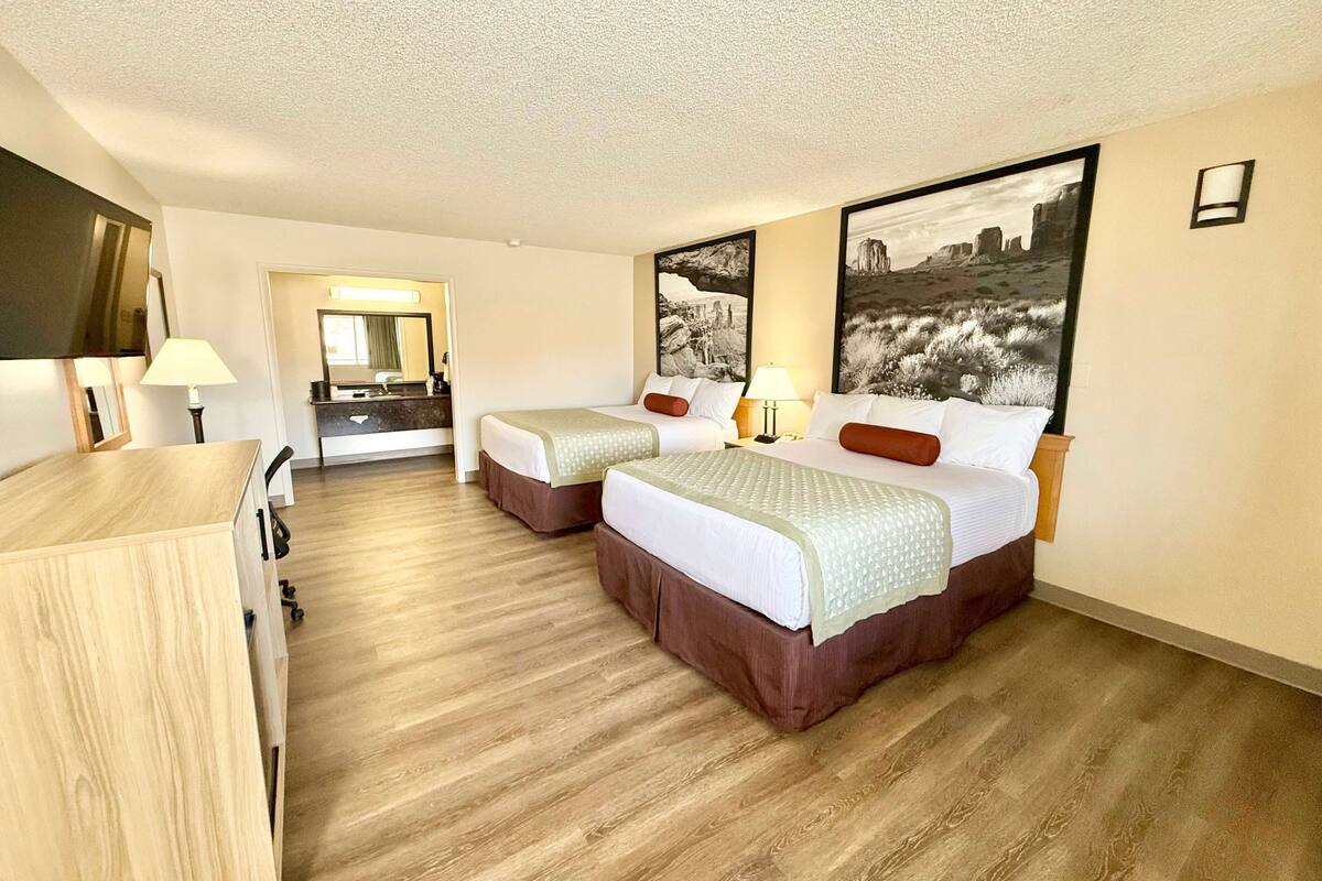 A hotel room with two beds, a desk, a mirror, and artwork on the walls.