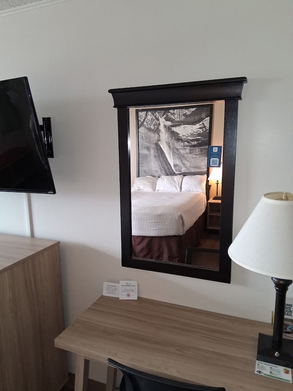 Habitación de hotel con una cama, un escritorio, una lámpara y un espejo que refleja el cuarto.