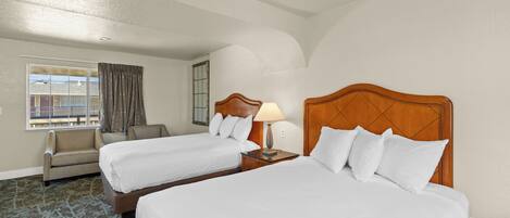 A hotel room with two beds, a chair, a lamp, and a window with curtains.