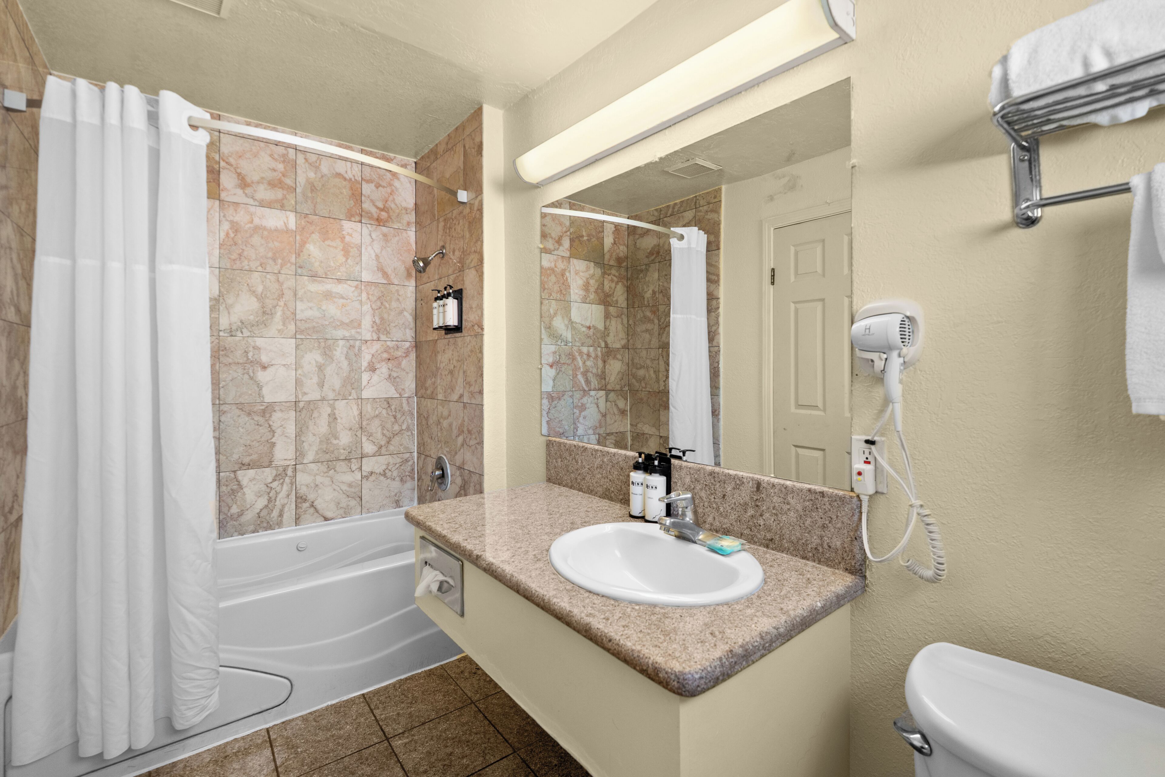 A bathroom with a bathtub, a sink, a toilet, and a hairdryer mounted on the wall.