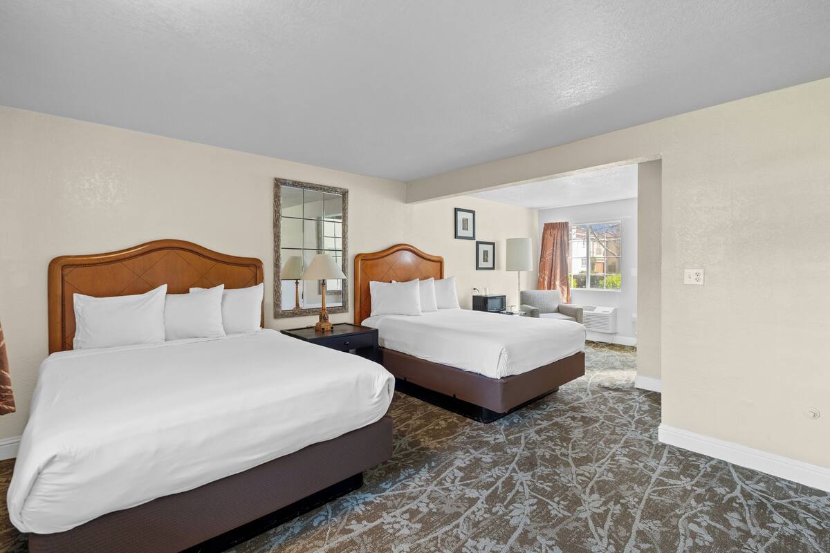 A hotel room with two beds, a large mirror, a desk with a lamp, and a view of the outdoors.