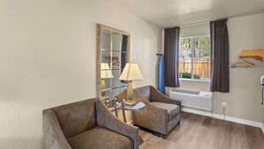 A room with two armchairs, a round table, a mirror, a window with curtains, and an air conditioning unit. - Rose Garden Inn - San Jose Airport (San Jose)