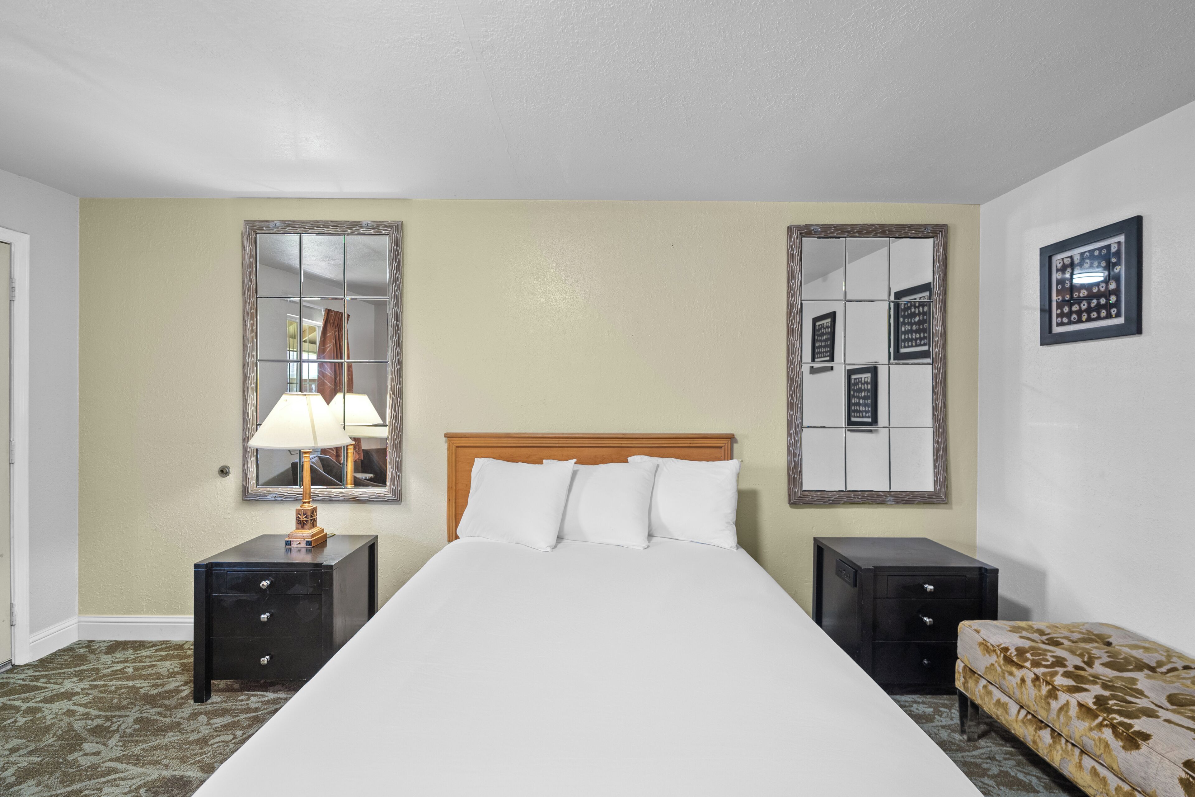A hotel room with a bed, two nightstands, a lamp, a mirror, and a sofa.