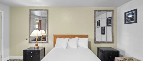 A hotel room with a bed, two nightstands, a lamp, a mirror, and a sofa.