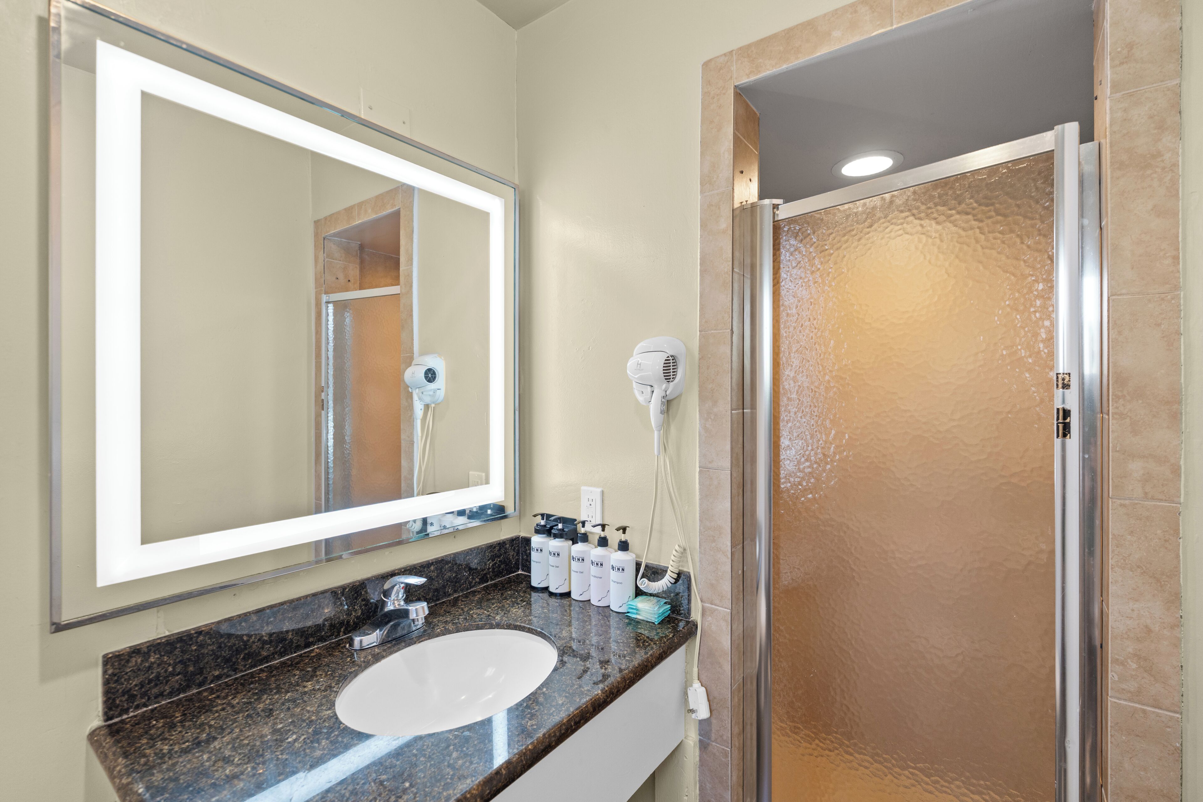 Une salle de bain équipée d’un lavabo, d’un miroir, d’un sèche-cheveux et d’une douche.