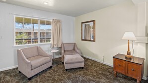A room with two armchairs, a small table, a lamp, a mirror, and a window with curtains. - Rose Garden Inn - San Jose Airport (San Jose)