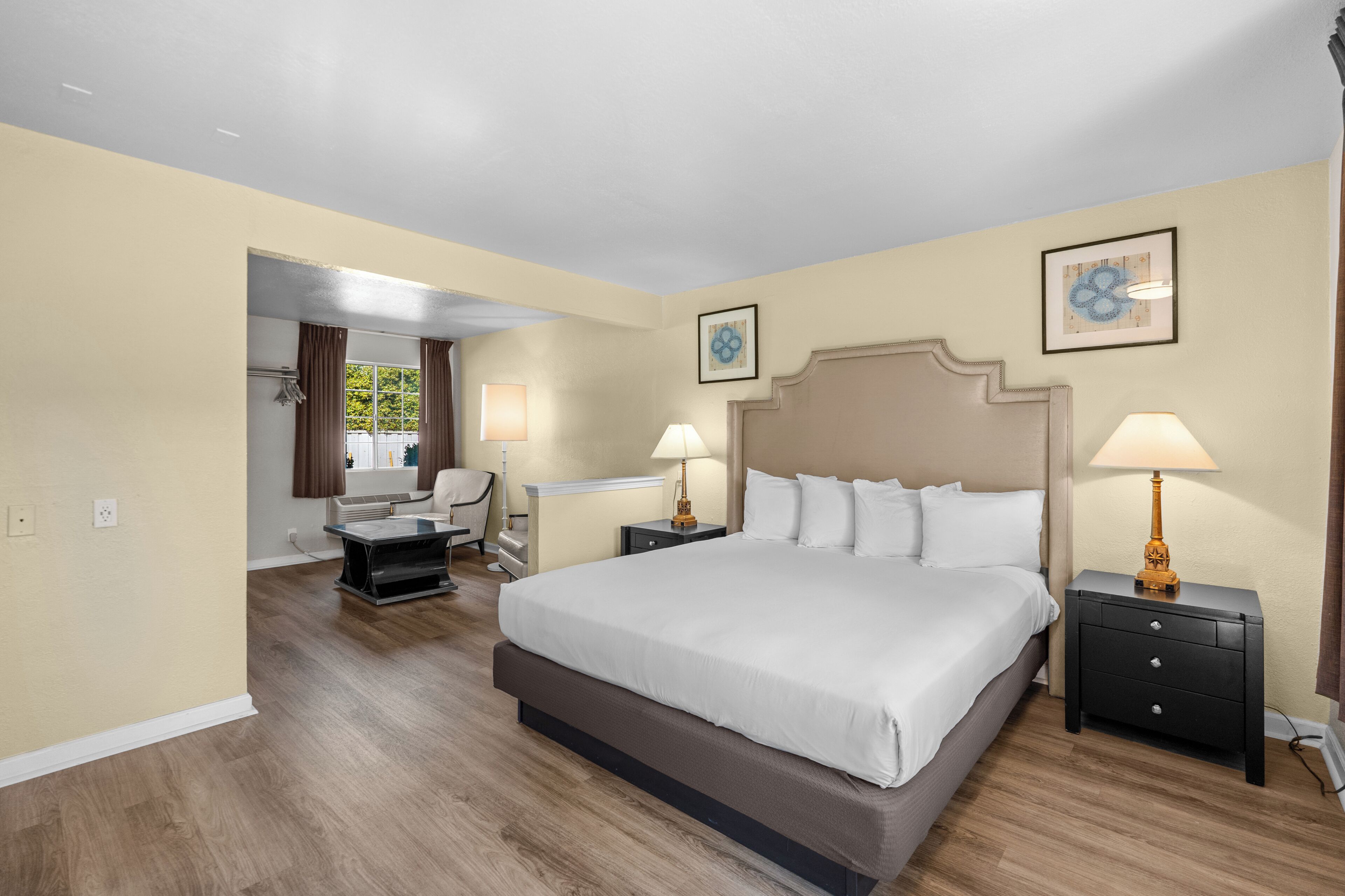 A hotel room with a large bed, two bedside tables with lamps, a chair, a desk, and a window with curtains.