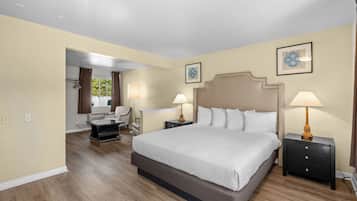 A hotel room with a large bed, two bedside tables with lamps, a chair, a desk, and a window with curtains.