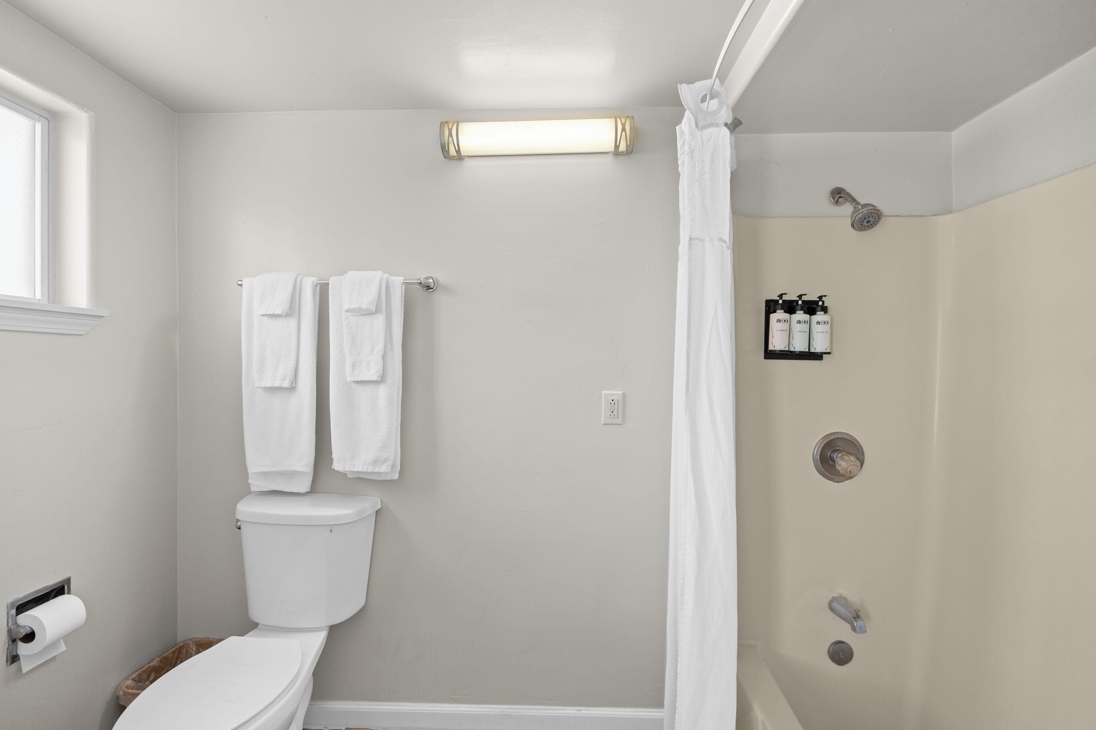 A bathroom with a toilet, a shower with a curtain, and a shelf with toiletries.