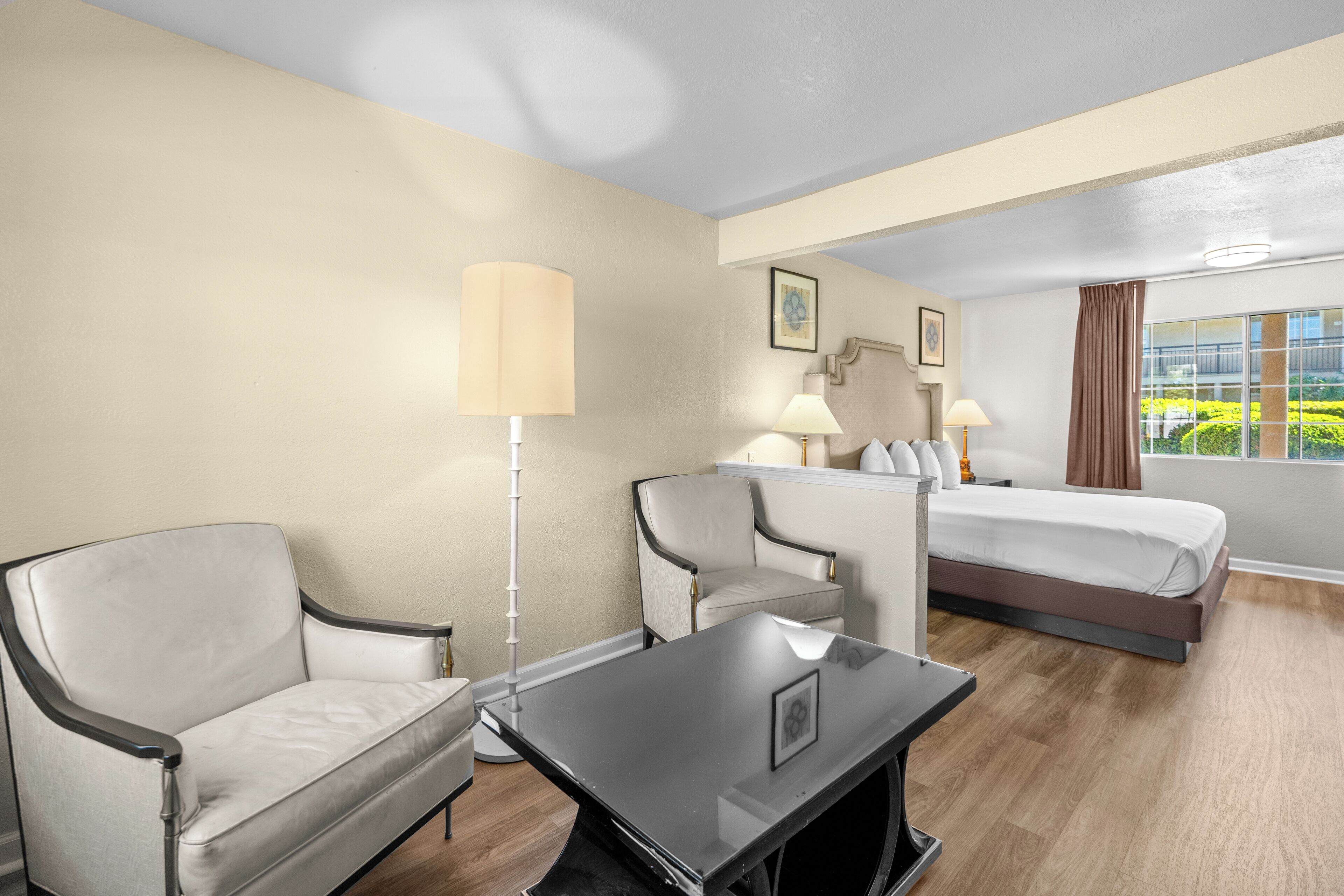 Una habitación de hotel con cama, escritorio, dos sillas, lámpara y ventana con vistas.