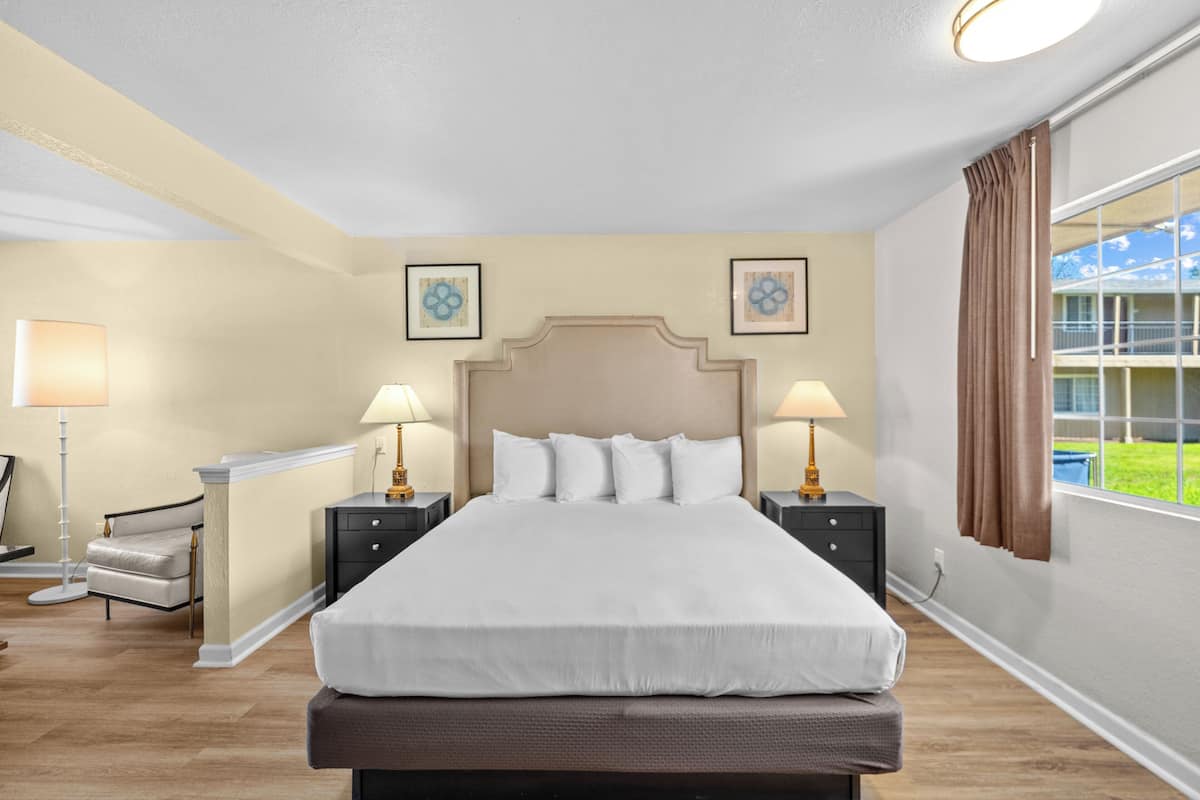 A hotel room with a large bed, bedside lamps, a chair, a nightstand, and a window with curtains.