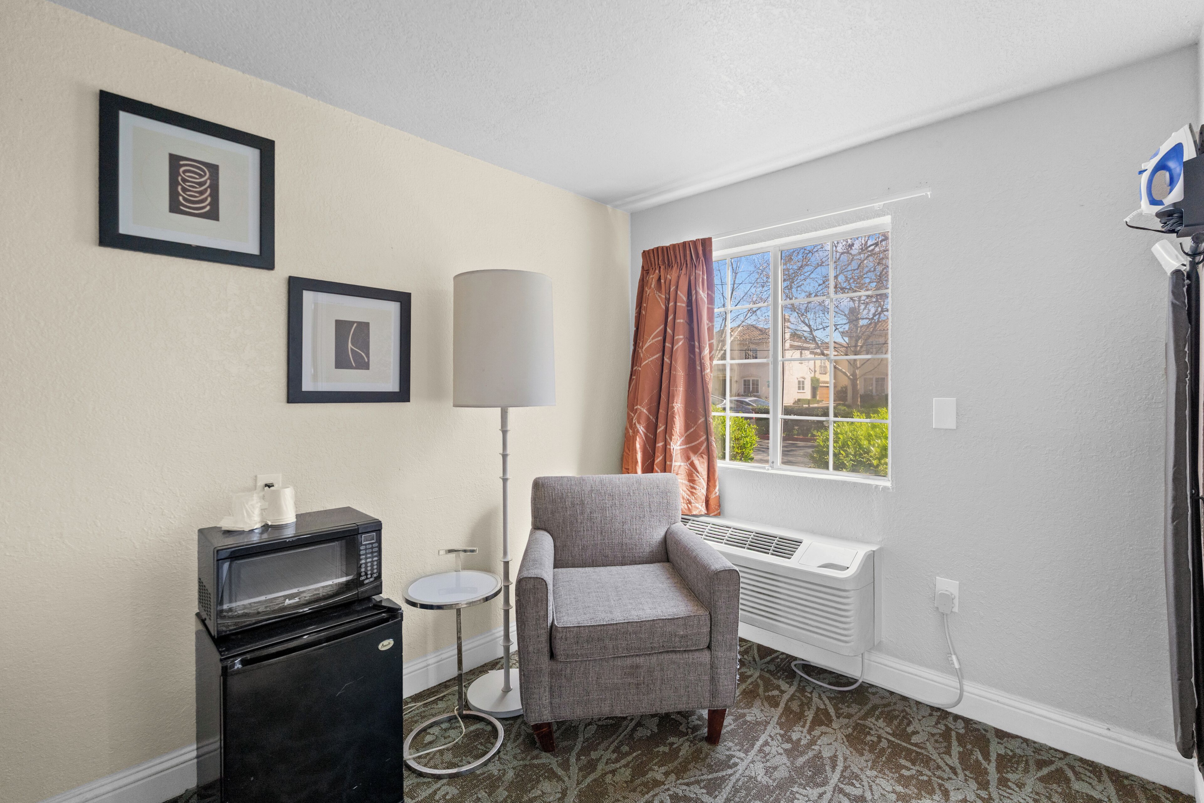 A room with a gray armchair, a black microwave, a floor lamp, and a window with a view of buildings.