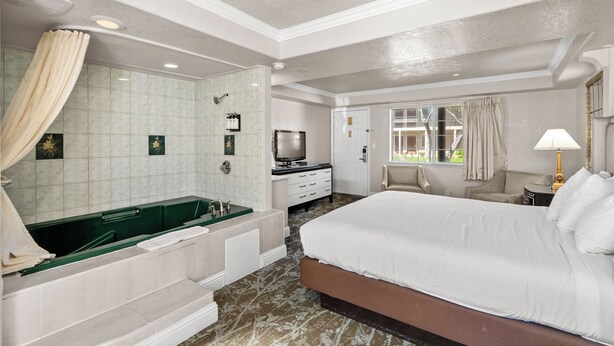 A hotel room with a large bed, a bathtub, a television, a desk, and a window with curtains. - Rose Garden Inn - San Jose Airport (San Jose)
