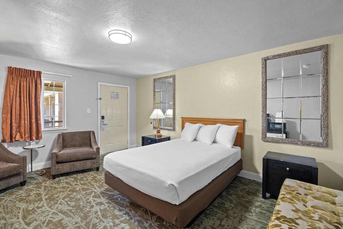 A hotel room with a bed, two nightstands, a chair, a mirror, and a door.