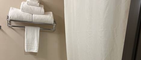 Un baño con inodoro, toallero con toallas dobladas y cortina de ducha.