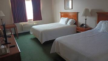 A hotel room with two beds, a desk, a chair, a lamp, and a window with curtains.