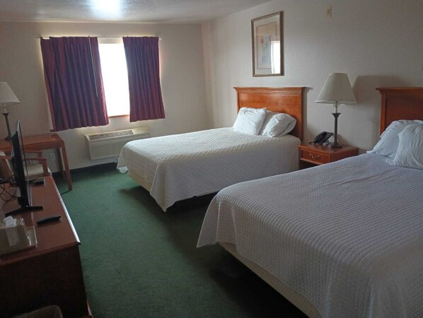 A hotel room with two beds, a desk, a chair, a lamp, and a window with curtains.