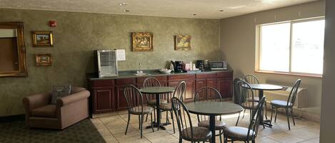 A spacious living area with a kitchen, dining table, and chairs. There are framed pictures on the wall, a refrigerator, and a microwave.