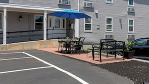 A covered outdoor seating area with tables and chairs, a blue umbrella, and a potted plant. - Westborough Inn (Westborough)
