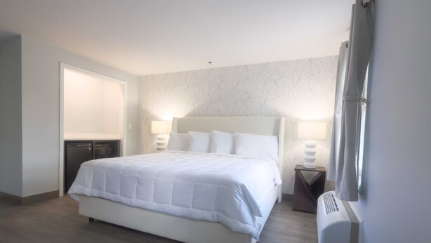 A neatly arranged hotel room with a large bed, bedside lamps, a heater, and a wardrobe. - Westborough Inn (Westborough)