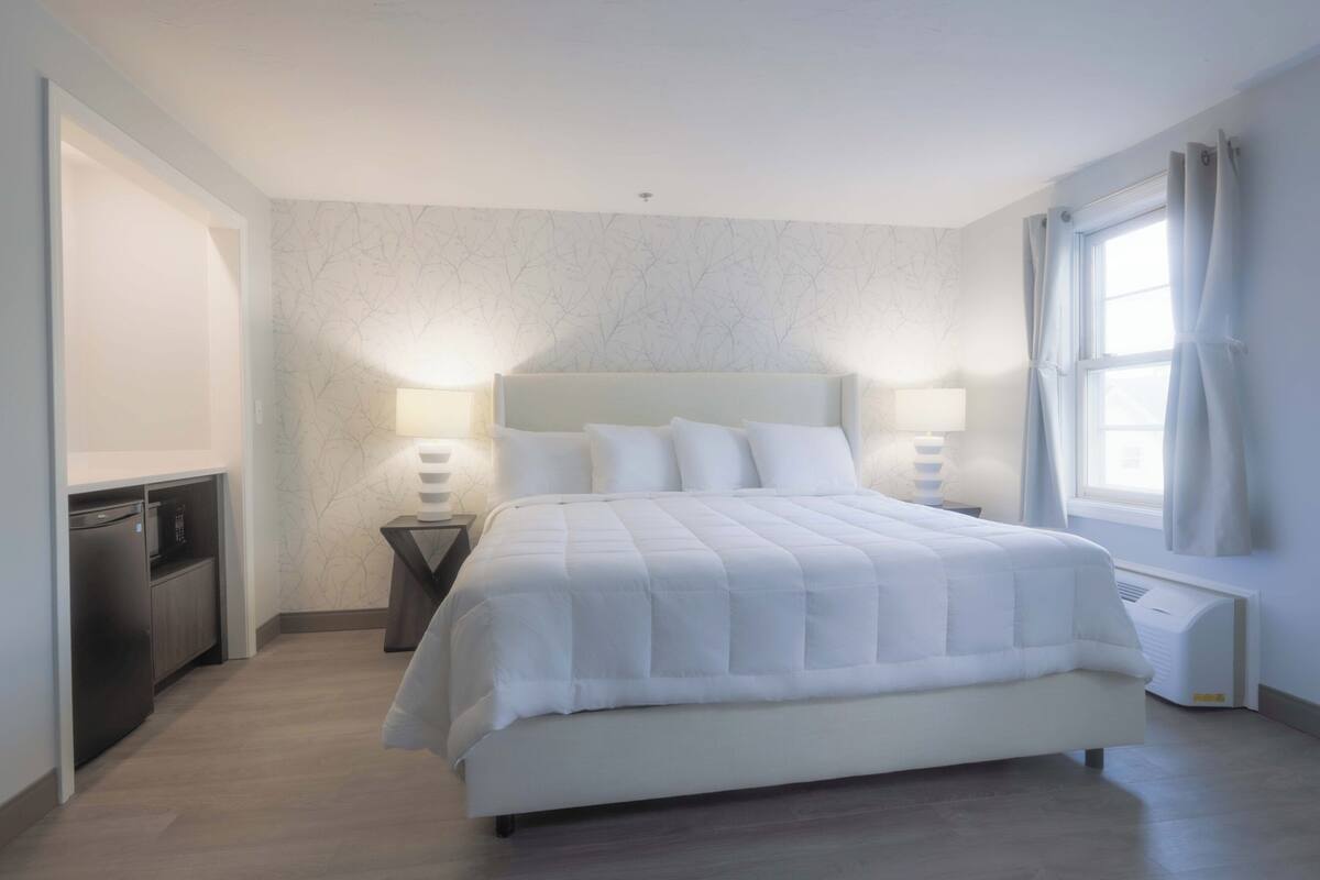 A modern bedroom with a large bed, bedside lamps, a built-in heater, and a view of the outdoors.