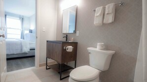 A bathroom with a toilet, a wooden vanity, a mirror, and a window.